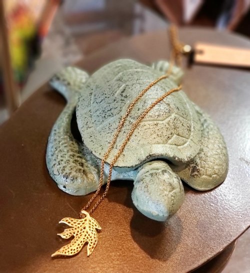 A decorative turtle sculpture with a gold leaf pendant necklace resting on it.