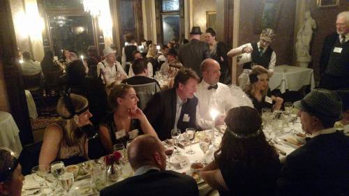 A lively dinner party scene with guests in formal attire, enjoying a meal at a beautifully set table.
