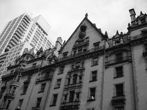 A historic building with ornate architecture, contrasted against a modern skyscraper in a black and white setting.