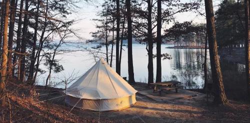A white tent by a calm lake, surrounded by trees, with a picnic table nearby and a serene landscape in the background.
