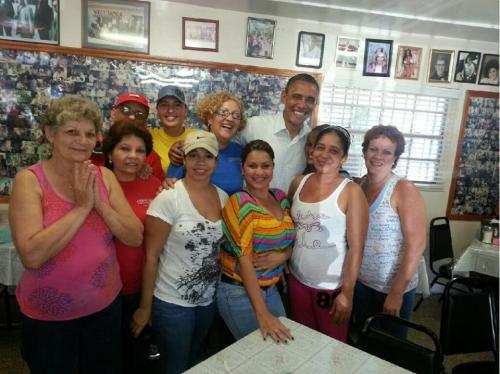 A group of people smiling together in a restaurant, with photos on the walls and a friendly atmosphere.