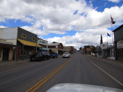 A small town street lined with shops and cars under a partly cloudy sky.