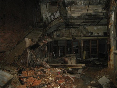 Interior of a dilapidated building with debris, crumbling walls, and a damaged staircase.