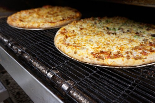 Two freshly baked pizzas on a grill, one topped with cheese and the other with various toppings, on a metal rack.