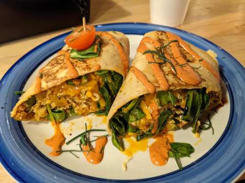 Two burritos on a blue plate, filled with greens, cheese, and sauce, garnished with a cherry tomato.