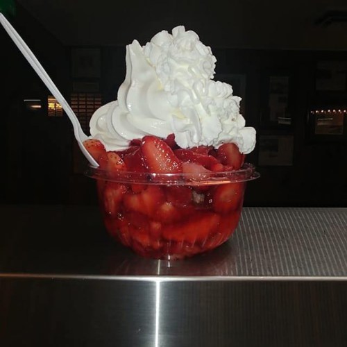 A clear cup filled with strawberries and topped with a generous swirl of whipped cream.