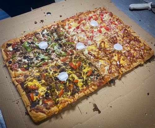 A large rectangular pizza divided into four sections, each with different toppings on a cardboard base.