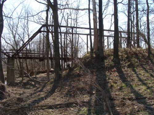 An abandoned, rusted structure partially hidden among bare trees and underbrush in a wooded area.