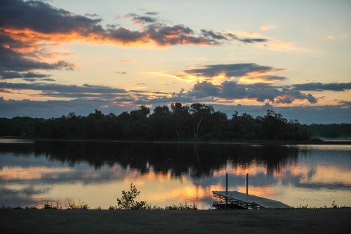 A serene lake at sunset, with colorful clouds reflecting on the water and a small dock in the foreground.