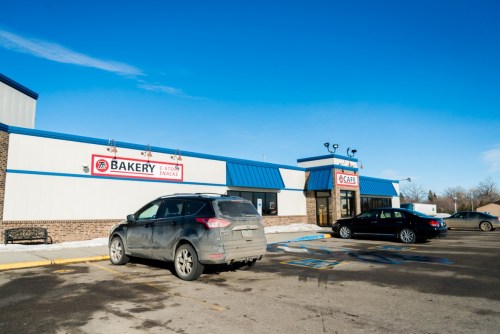 A bakery and café building with a blue roof, featuring parked cars in front and a clear blue sky above.