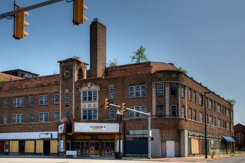 Abandoned brick building with boarded windows, a tall chimney, and a traffic light in the foreground.