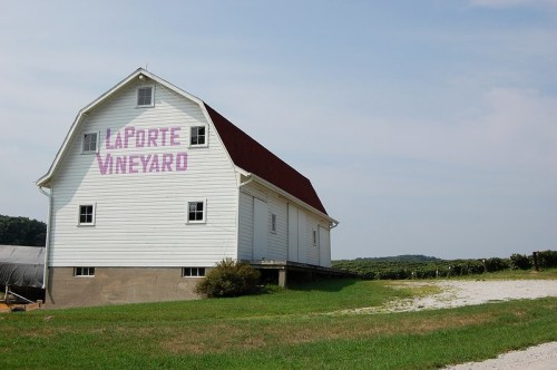 A white barn with a red roof, labeled "LaPorte Vineyard," set against a clear sky and green landscape.
