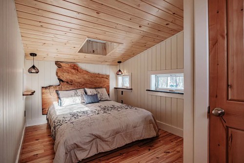 Cozy bedroom with wooden ceiling, a large wood accent wall, and a bed adorned with floral bedding and soft lighting.