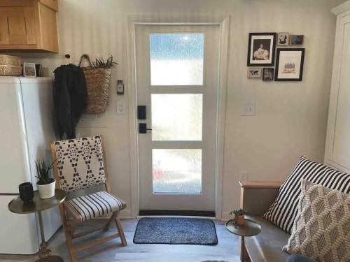 Cozy entryway with a door, chair, small table, and framed photos on the wall, featuring light and neutral decor.