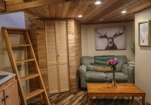 Cozy living space with wooden walls, a green couch, a wooden table, and a staircase leading to a loft area.