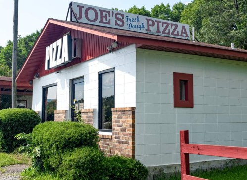 Exterior of Joe's Fresh Dough Pizza, featuring a red roof, white walls, and a sign with "PIZZA" prominently displayed.
