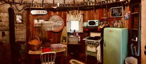 Cozy vintage kitchen with a green fridge, stove, wooden table, and rustic decor, featuring a Coca-Cola sign.