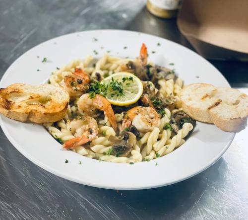 A plate of pasta with shrimp, mushrooms, and lemon, garnished with parsley, served with two slices of toasted bread.