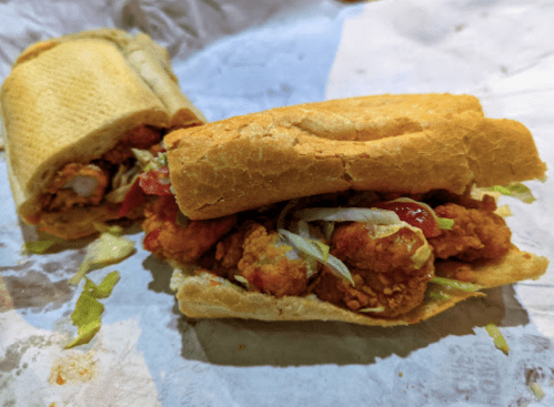A close-up of a sandwich filled with fried chicken, lettuce, and sauce, resting on crumpled paper.
