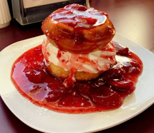 A stacked dessert featuring two donuts filled with cream and topped with strawberry sauce on a white plate.