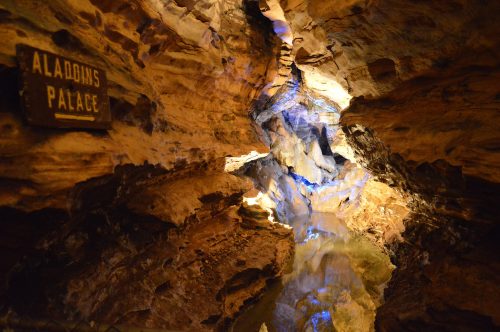 A dimly lit cave with rock formations and a reflective pool, featuring a sign that reads "Aladdin's Palace."