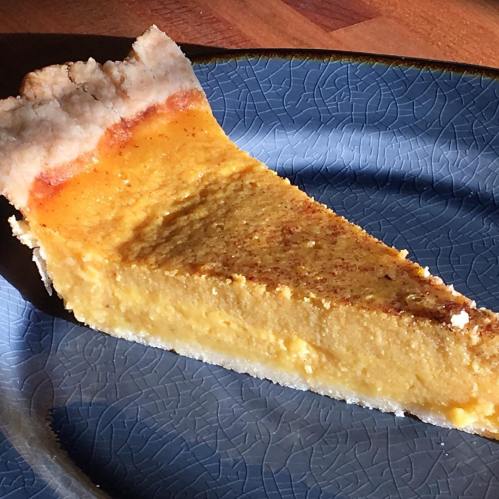 A slice of pumpkin pie on a blue plate, showcasing a smooth, creamy filling and a golden-brown crust.