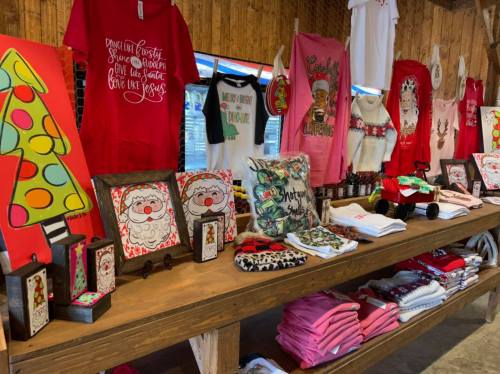 A festive display of holiday-themed clothing and decorations on a wooden table, featuring shirts, prints, and ornaments.