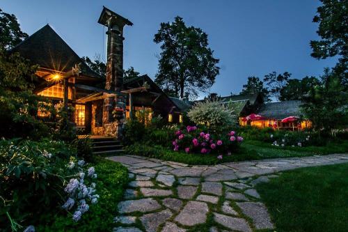 A charming lodge at dusk, surrounded by lush gardens and colorful flowers, with warm lights glowing from the windows.