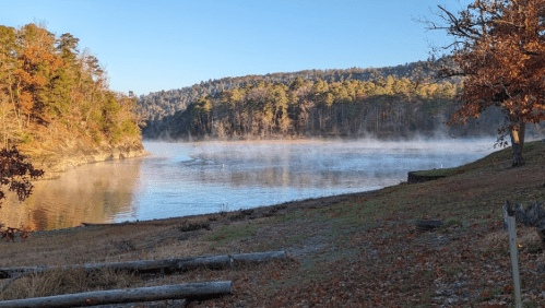 A serene lake surrounded by autumn trees, with mist rising from the water under a clear blue sky.