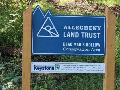 Sign for Allegheny Land Trust at Dead Man's Hollow Conservation Area, featuring mountains and a scenic logo.