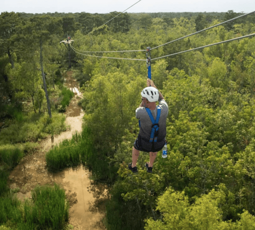 A person in a helmet zip-lining over a lush green landscape with a winding creek below.