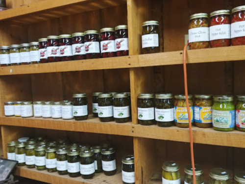 Shelves filled with jars of various pickled vegetables and hot sauces, labeled with names and ingredients.