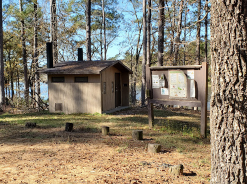 A small wooden building and an information board surrounded by trees in a natural setting.