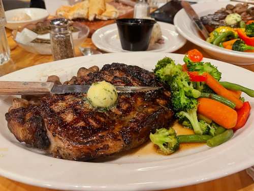 A grilled steak topped with butter, served with a side of mixed vegetables including broccoli and carrots.