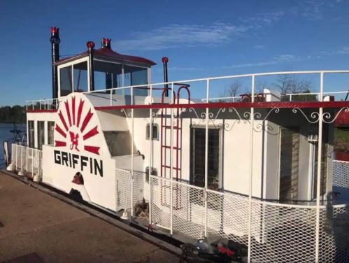 A white and red riverboat named "Griffin" docked by the water, featuring a sunburst design and multiple levels.
