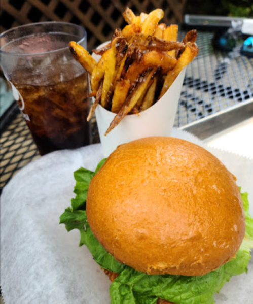 A crispy chicken sandwich with lettuce, served with a side of fries and a glass of cola on a table.