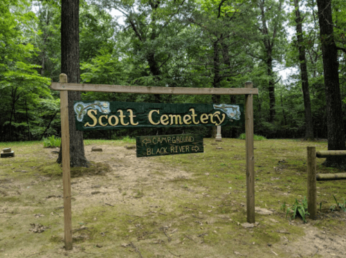 Sign for Scott Cemetery surrounded by trees, with directions to Campground and Black River.