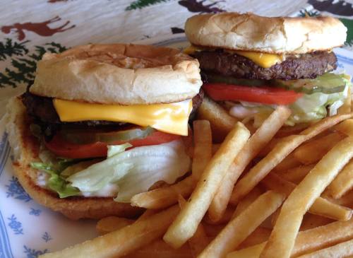Two cheeseburgers with lettuce, tomato, and pickles, served with a side of golden French fries on a plate.