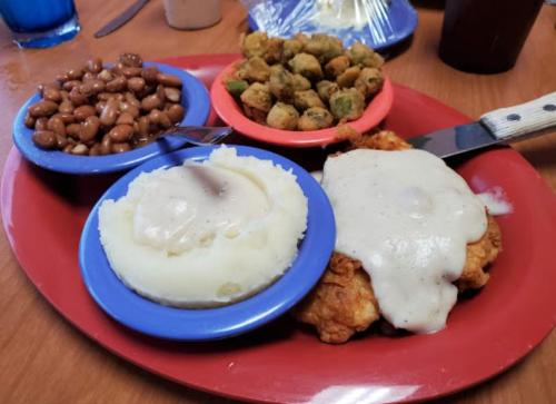 A red plate with fried chicken topped with gravy, mashed potatoes, baked beans, and fried okra.