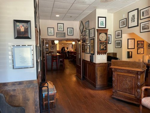 A cozy restaurant interior with wooden accents, framed photos on the walls, and a glimpse of the dining area.