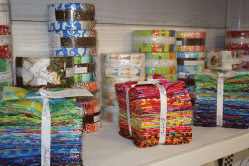 Colorful rolls and stacks of fabric strips neatly arranged on shelves, showcasing various patterns and designs.