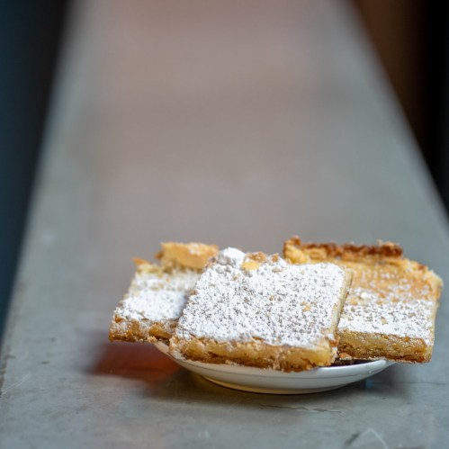 A plate of three powdered sugar-dusted dessert bars on a gray surface.