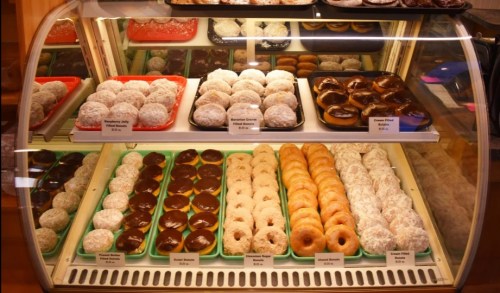 A display case filled with various donuts, including glazed, chocolate-covered, and powdered sugar varieties.