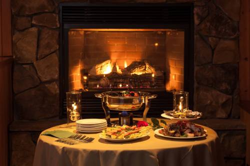 A cozy dining setup with a table of assorted dishes in front of a warm fireplace, creating an inviting atmosphere.