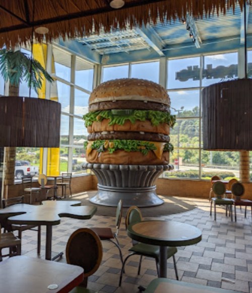 A giant hamburger sculpture inside a restaurant, surrounded by tables and large windows.