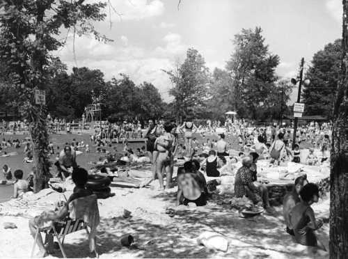 A crowded beach scene with people swimming, lounging, and enjoying the sun under a bright sky.