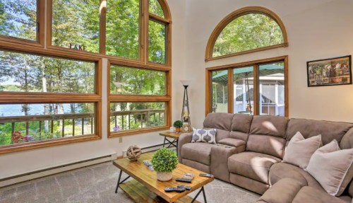 Cozy living room with large windows, a sectional sofa, and a coffee table, overlooking a serene outdoor view.