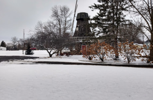 A snowy landscape featuring a windmill and bare trees, with a cloudy sky overhead.