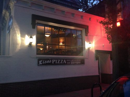 Exterior of Lisa's Pizza restaurant at dusk, featuring a large window and a sign with the phone number.