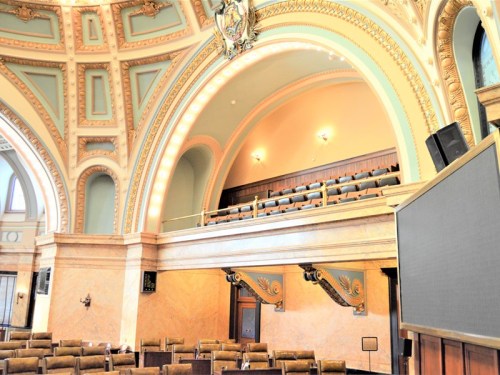 Interior of a grand hall featuring ornate arches, decorative details, and seating areas.